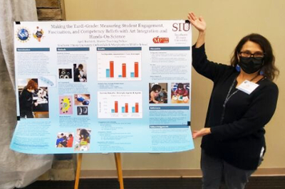 April Bartnick standing next to her conference poster titled, "Making the Tardi-Grade: Measuring Student Engagement, Fascination, and Competency Beliefs with Art Integration and Hands-On Science"
