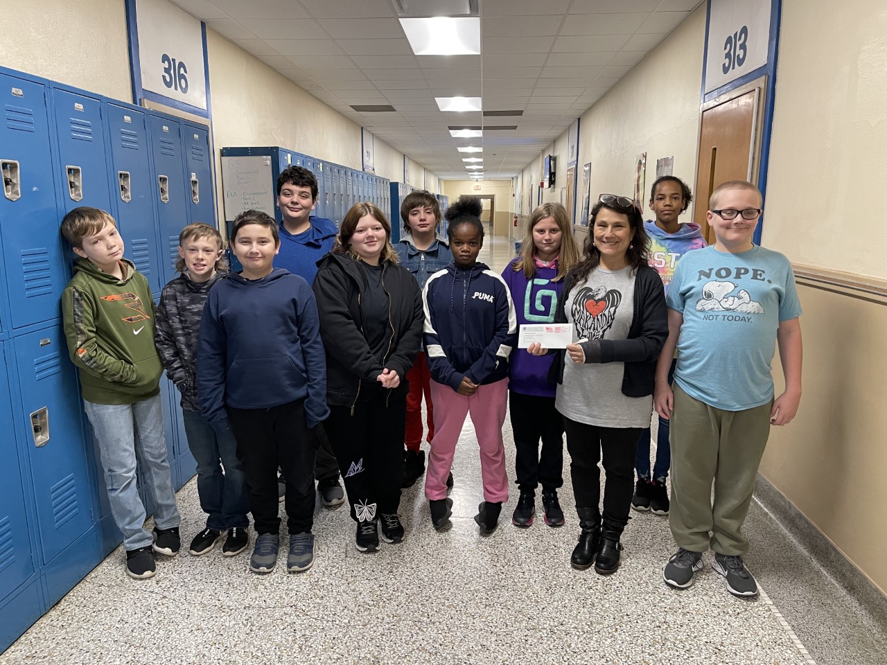 Photo of April Bartnick and her sixth grade class standing in a hallway proudly displaying the grant check.
