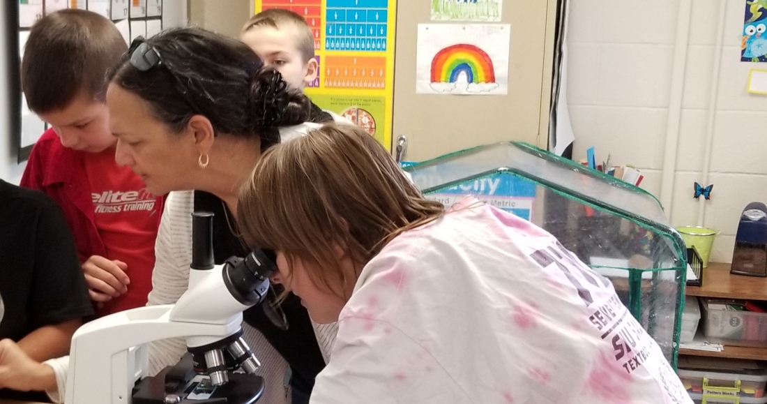 Photo of Renee helping students with microscopes